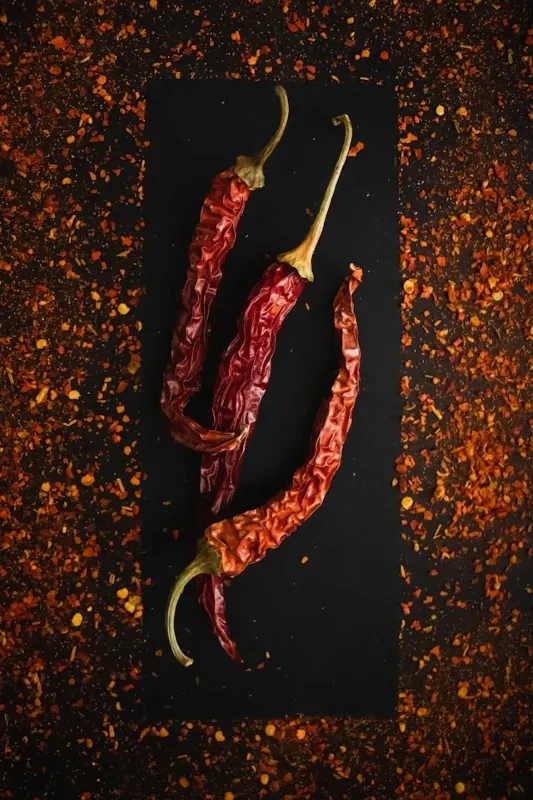 Getrocknete rote Chilischoten auf dunklem Untergrund mit Chiliflocken