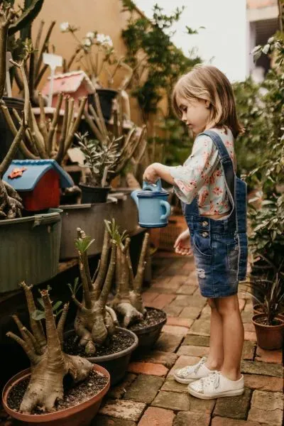 Kind gießt Topfpflanzen in einem kleinen Gartenhof