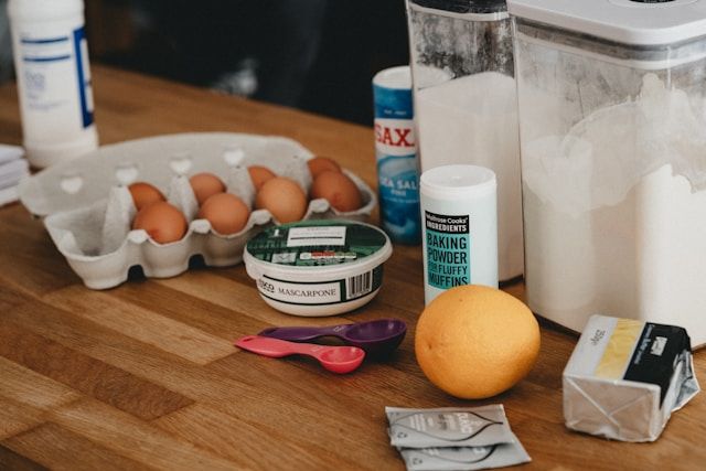 Backzutaten mit Eiern, Mehl, Mascarpone, Butter und Backpulver auf Holzarbeitsfläche